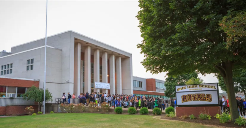 L'edificio della Erie High School con grandi colonne all'ingresso, studenti radunati e un cartello con il nome della scuola.