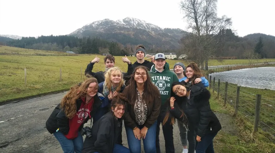 Un gruppo di studenti della Acton High School si trova insieme in una suggestiva area all'aperto con montagne e alberi sullo sfondo.