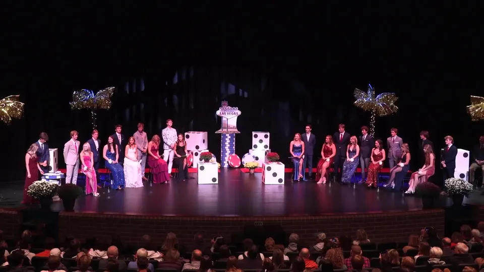 Gli studenti della Rockford High School si esibiscono in abiti sgargianti con elaborati copricapi su un palco con uno sfondo decorativo.