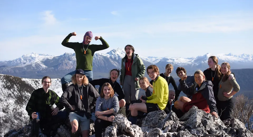Un gruppo di studenti della Hobart City High School posa su una roccia con montagne innevate sullo sfondo.