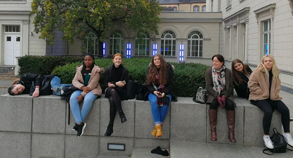 Un gruppo di studentesse è seduto su un muretto in pietra davanti a un edificio con finestre ad arco nel terreno della Denefield School.