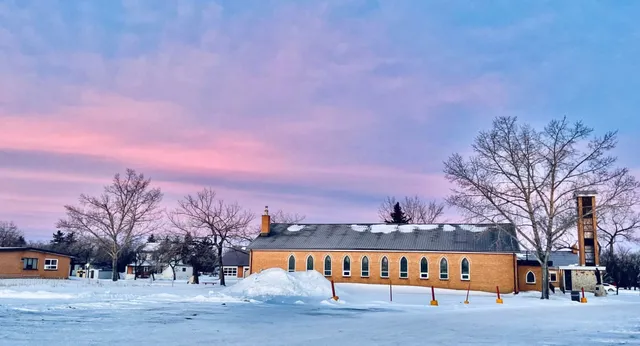 L'Athol Murray College of Notre Dame mostra un edificio in mattoni con un bosco invernale innevato e un cielo colorato sullo sfondo.