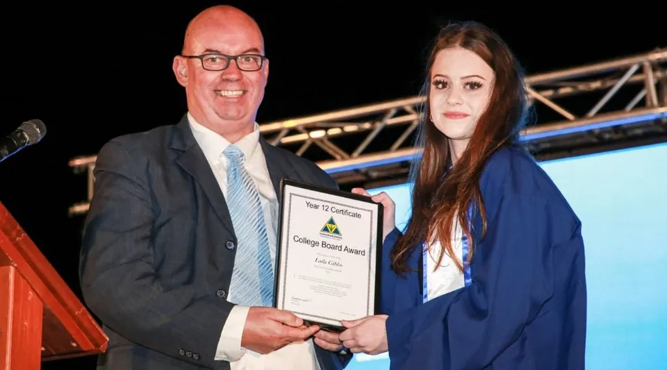 Un uomo e una donna in abito formale durante la consegna di un certificato nel campus del Wanneroo Secondary College.