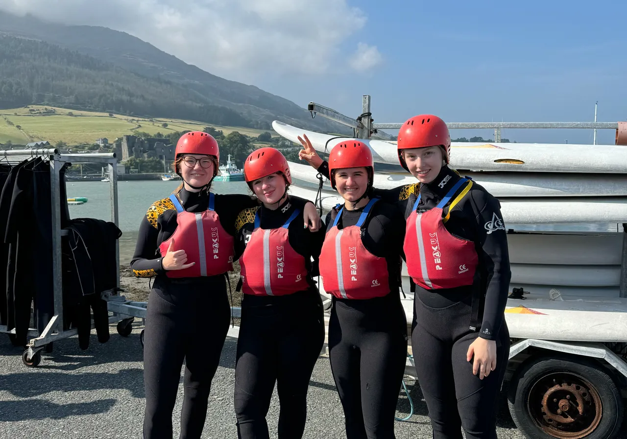 Cuatro chicas con traje de neopreno, casco y chaleco salvavidas en un centro de deportes acuáticos