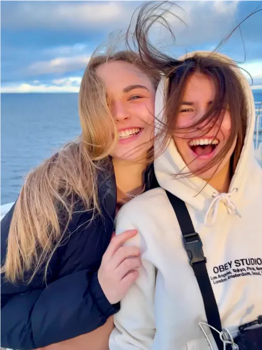 Zwei Mädchen lachen auf einem Boot vor Meer und bewölktem Himmel in Kanada