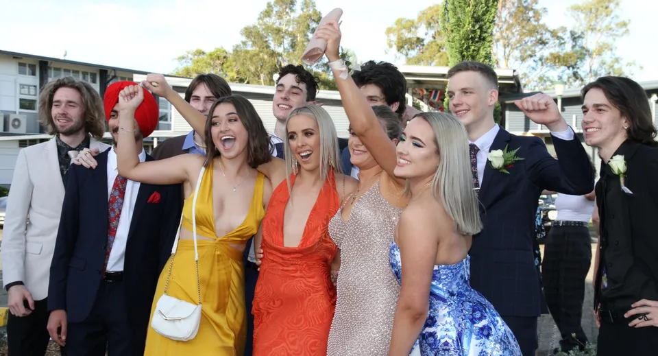 Un gruppo di studenti della Kedron State High School festeggia insieme davanti agli edifici scolastici e agli alberi.