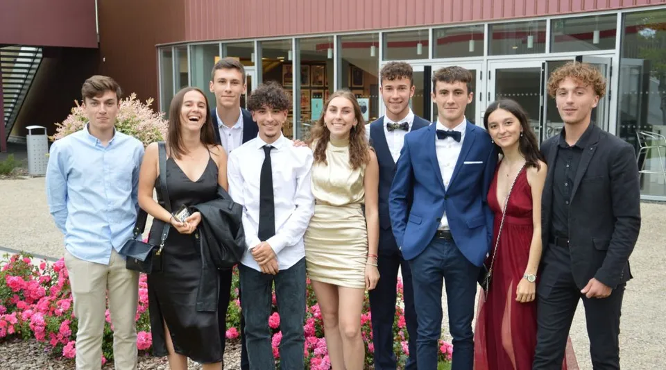 Un gruppo di studenti e studentesse del Lycée Charles Péguy in abito formale sta davanti a un edificio rosa.