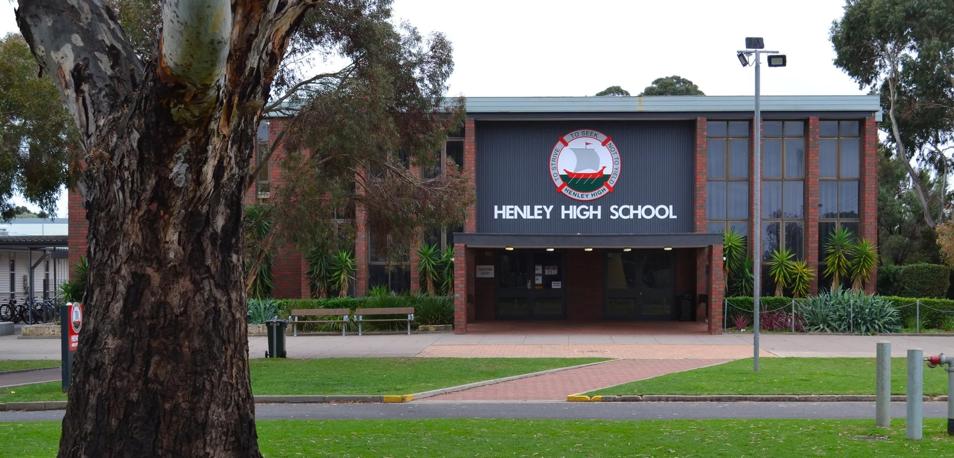 L'ingresso dell'edificio in mattoni della Henley High School con un grande cartello e alberi in primo piano.