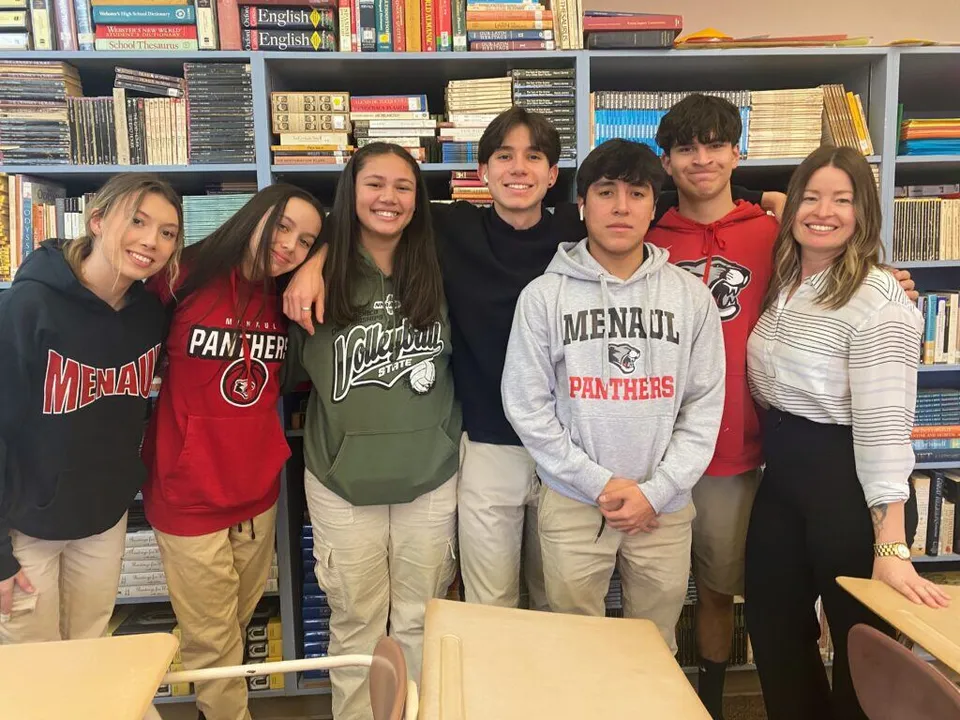 Un gruppo di studenti della Menaul School in posa insieme davanti a scaffali di libri in una biblioteca scolastica.