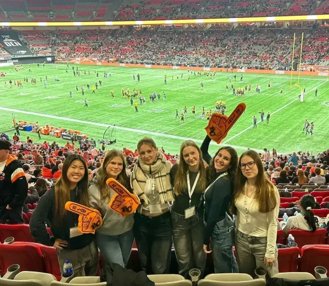 Gruppo di studentesse con dita di gomma da tifosi assiste a una partita di football in uno stadio canadese