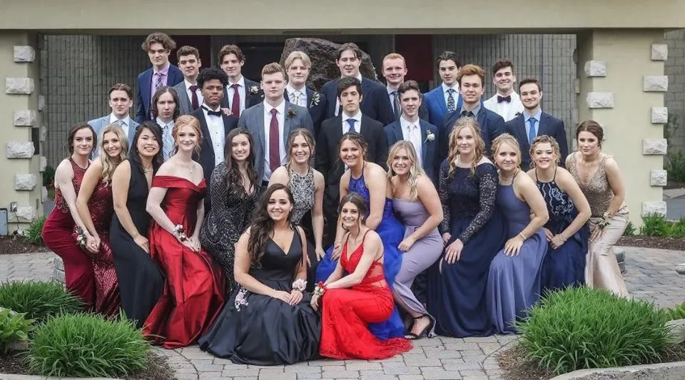 Un gruppo di persone vestite in modo formale posa all'esterno della Ontario Hockey Academy su un viale pavimentato con aree verdi sullo sfondo.