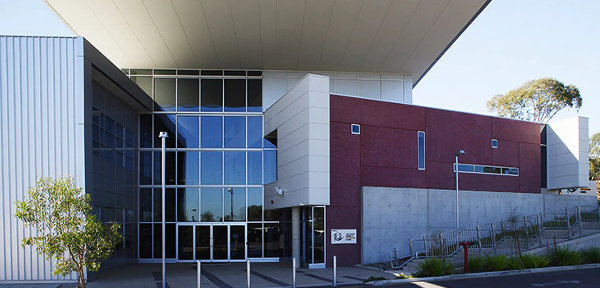 L'edificio principale moderno della Australian Science and Mathematics School con ingresso in vetro e ringhiera in metallo, circondato da alberi e un prato.