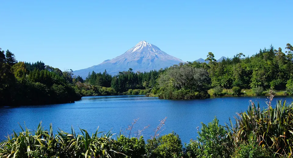 Un lago calmo con vegetazione verde sulla riva e una montagna innevata sullo sfondo nei pressi del Sacred Heart Girls' College a New Plymouth.