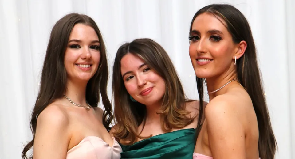 Tre studentesse dell'Ursuline College Sligo posano insieme davanti a uno sfondo bianco in abiti formali.