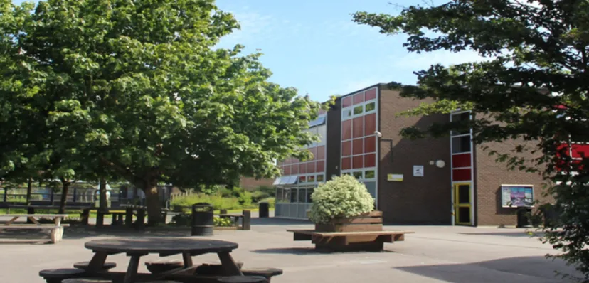 Il cortile interno della Ferndown Upper School mostra panchine di legno davanti a un edificio in mattoni ed è circondato da alberi.