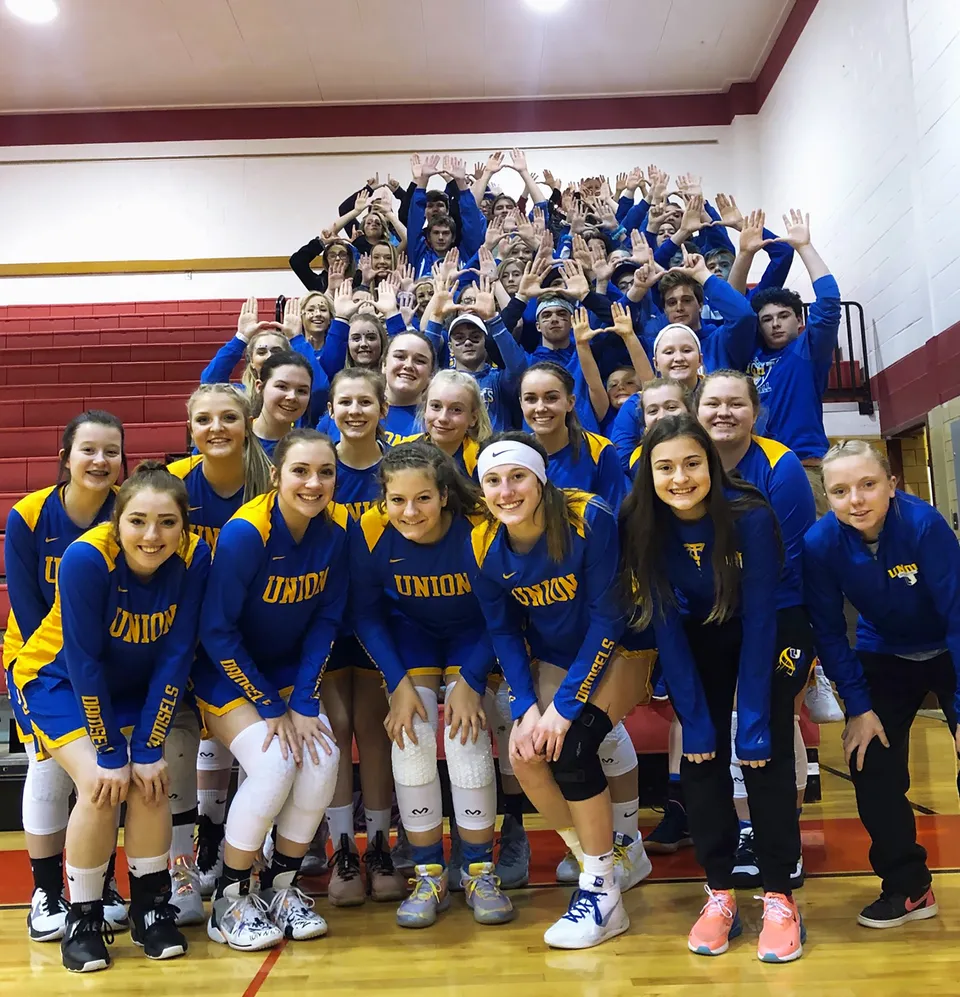 Un gruppo di studentesse della Union High School si trova insieme in uniformi blu e gialle in una palestra.