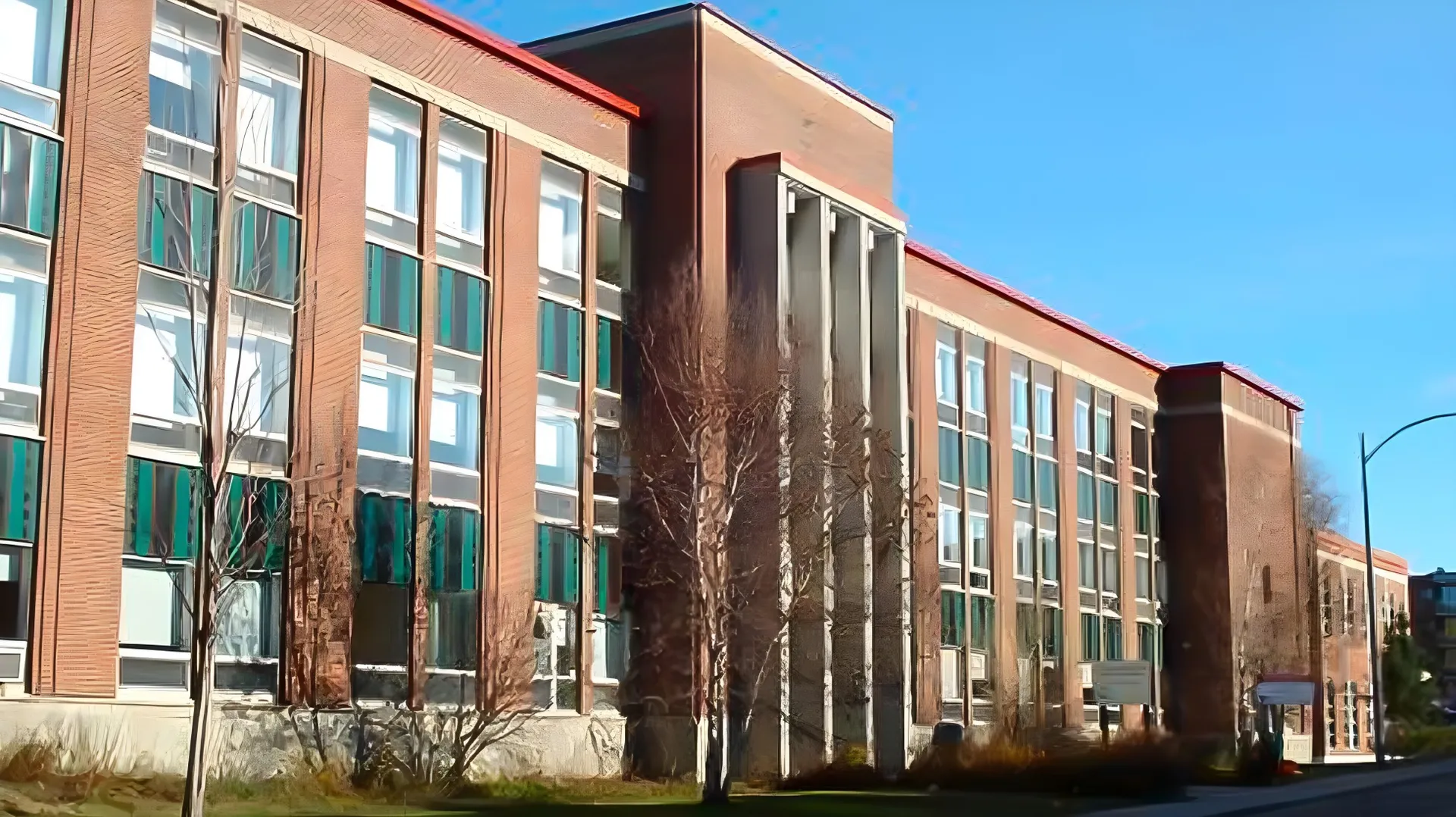 L'edificio in mattoni a più piani della Québec High School con grandi finestre e un ingresso caratteristico sotto un cielo azzurro e limpido.