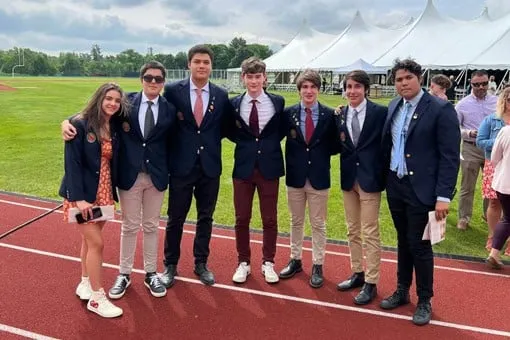 Siete estudiantes vestidos con chaqueta posan juntos sobre una pista de atletismo