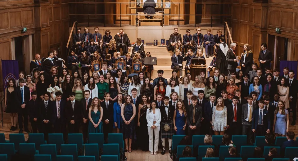 Un grande gruppo di diplomati della St. Leonards School si riunisce in un sontuoso auditorium per la cerimonia di diploma.