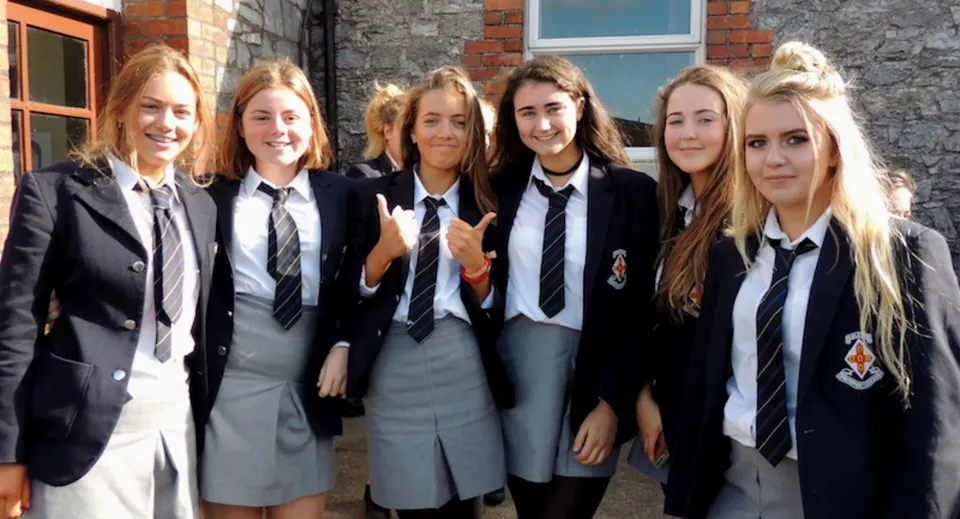 Un gruppo di sei studentesse in uniforme scolastica si trova davanti a un edificio in mattoni nel campus del Midleton College.