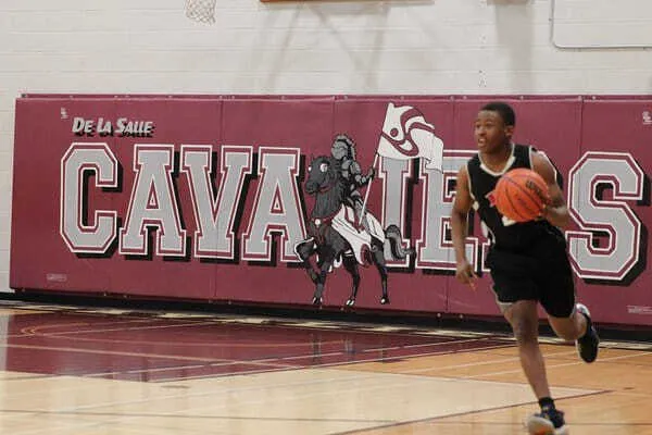 Un deportista está en la cancha de baloncesto con un gran mural de De La Salle Cavaliers al fondo en el campus de la École secondaire publique De La Salle.