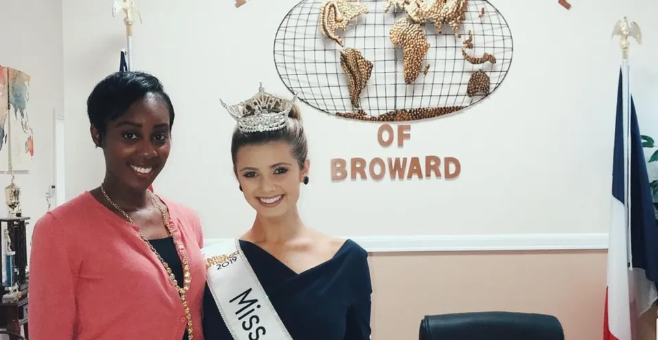 Due donne posano davanti a uno sfondo con la scritta della International School of Broward.