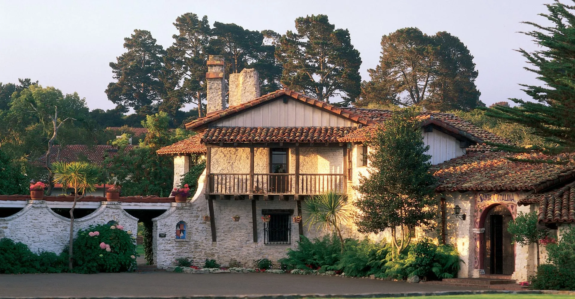 Una casa rustica con tetto in tegole circondata da una rigogliosa vegetazione e alti pini nel campus della Santa Catalina School.