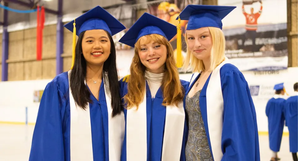 Tre studentesse in toga blu da diploma festeggiano il loro successo alla Brooks Secondary School.