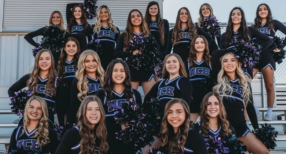 Un gruppo di cheerleader con divise abbinate posa davanti a una struttura metallica nel campus della Northwest Christian High School.