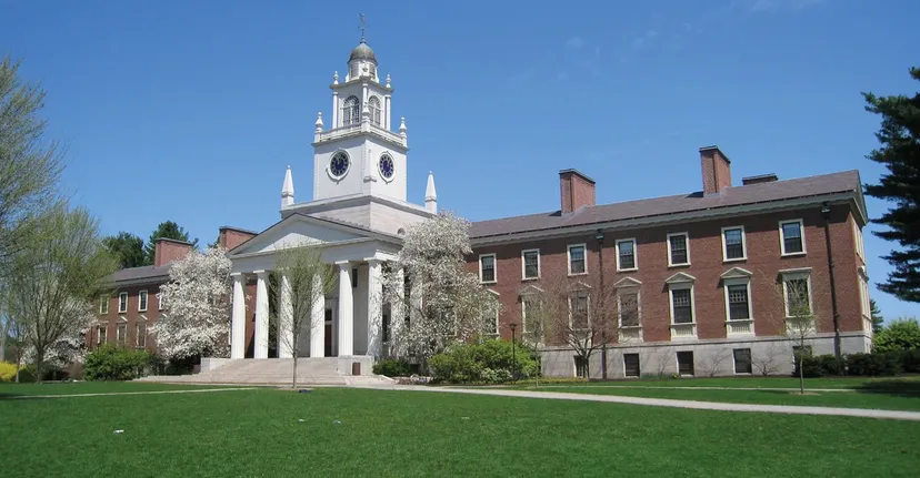 L'edificio storico con un'alta torre dell'orologio nel campus della Phillips Academy è circondato da alberi verdi e piante in fiore.
