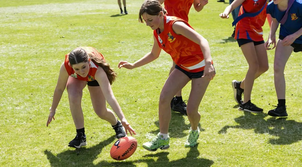 Due studentesse della Eastern Hills Senior High School giocano su un campo sportivo, sullo sfondo si vedono altre persone.