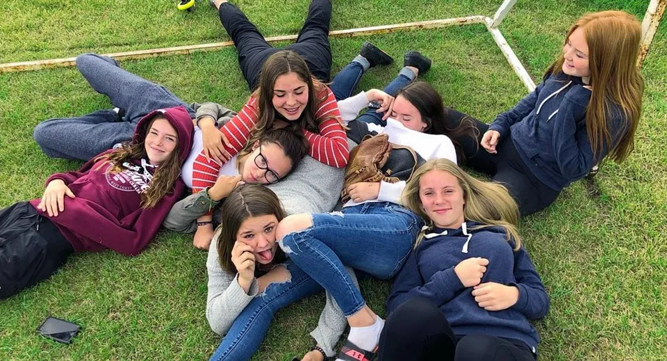 Un gruppo di studentesse della Nechako Valley Secondary School è sdraiato sull'erba e si abbraccia all'aperto.