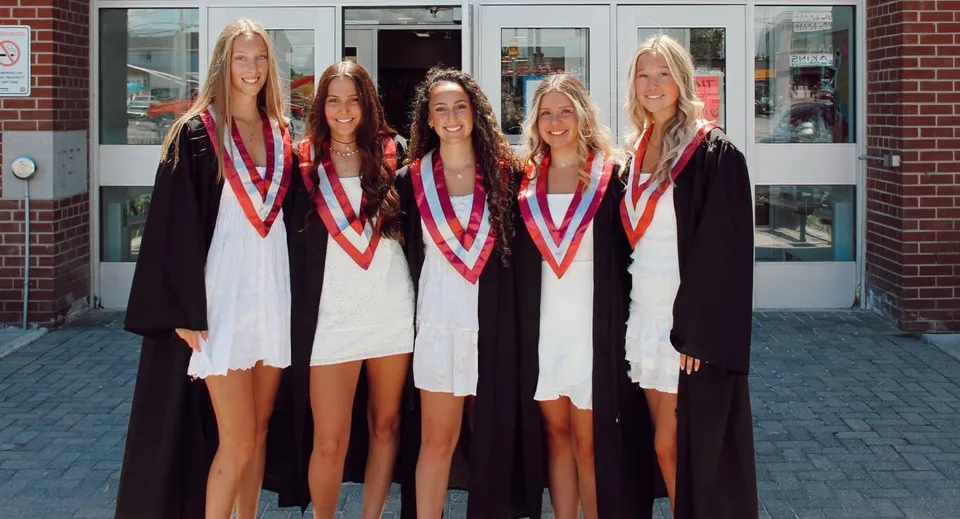 Cinque diplomate sono davanti a un edificio in mattoni nel campus della Frontenac Secondary School e festeggiano il loro diploma.