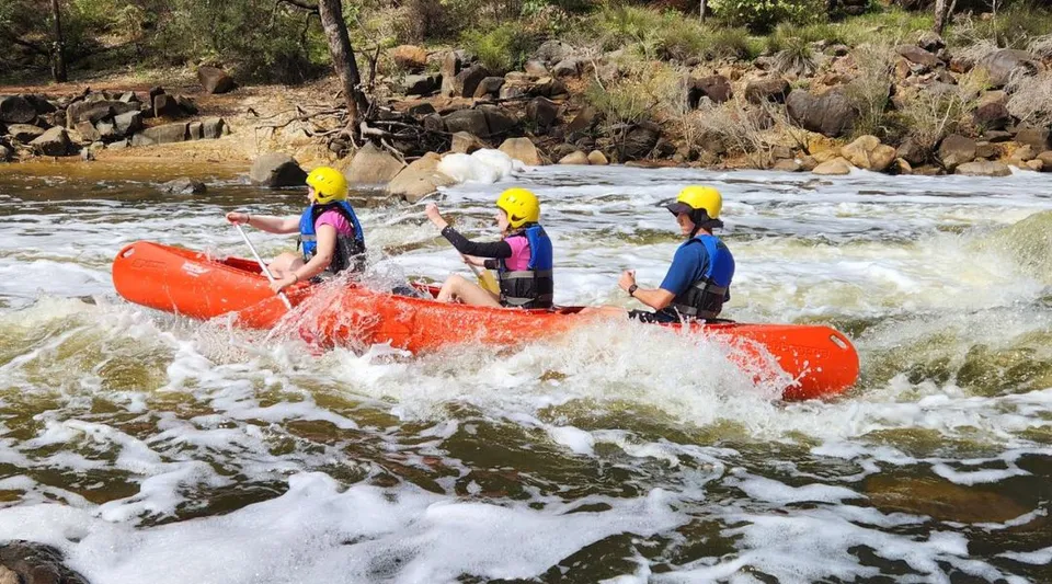 Studenti del Greenwood College guidano un gommone rosso su un fiume impetuoso indossando giubbotti di salvataggio colorati e caschi.