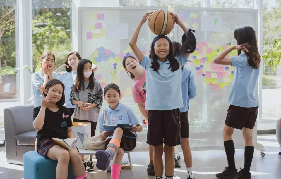 Eine Gruppe junger Schülerinnen der North London Collegiate School Jeju steht in einem Raum mit bunten Sticky Notes, dabei hält eine Schülerin einen Basketball.