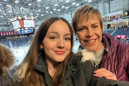 Una chica y una mujer sonríen a la cámara en un estadio de hockey cubierto
