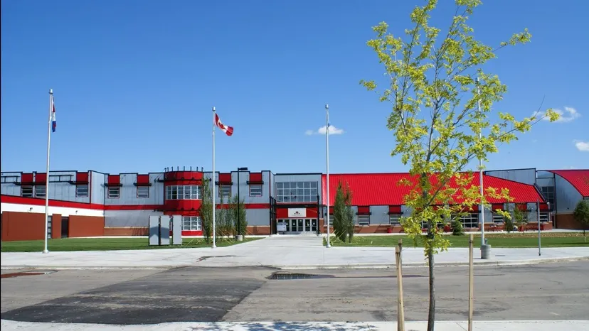 L'edificio moderno della Lindsay Thurber Comprehensive High School con bandiere al vento e alberi in primo piano.