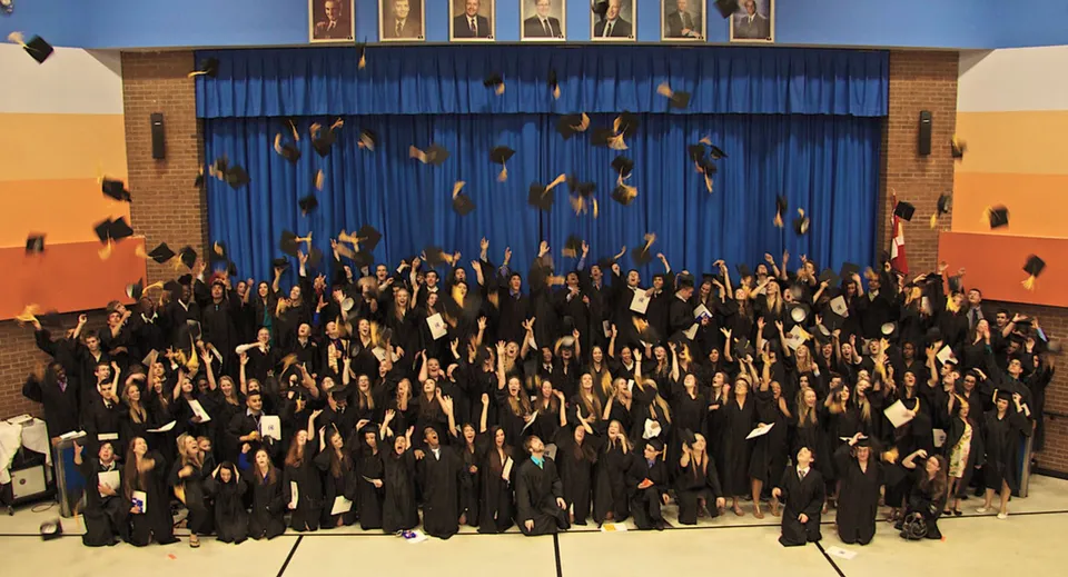 I diplomati della Cairine Wilson Secondary School festeggiano il loro diploma davanti a un palcoscenico con tende blu.