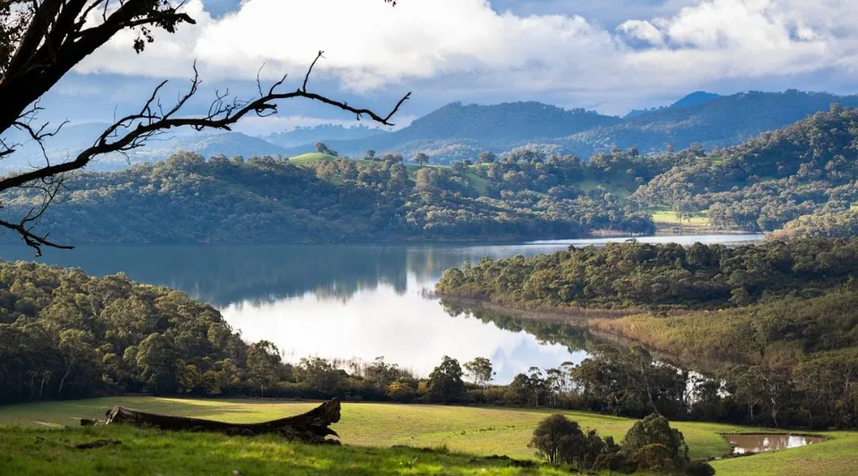 Un lago tranquillo con colline verdi e montagne, ripreso vicino alla Balga Senior High School.