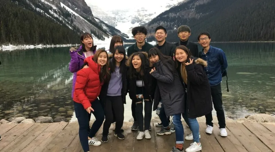 Un gruppo di persone si trova su un pontile di legno davanti a un paesaggio montano con lago nei pressi della Viking School.