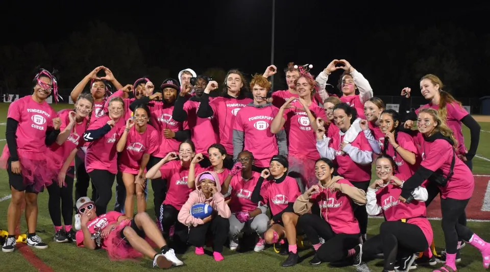Un grande gruppo di giovani donne con magliette rosa abbinate si trova all'aperto di notte nel campus della Vacaville Christian School.