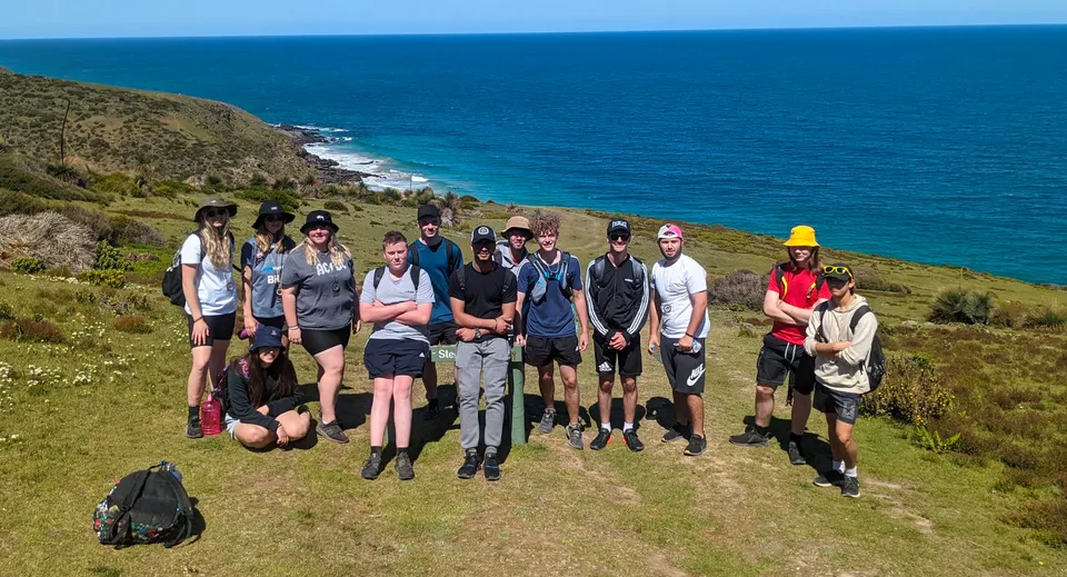 Un gruppo di studenti della The Heights School si trova su un'altura verde con vista sul mare blu e sulla costa rocciosa.