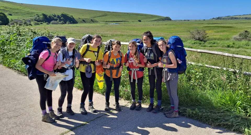 Un gruppo di studenti e studentesse della Benenden School sta in piedi su un prato con le montagne sullo sfondo.