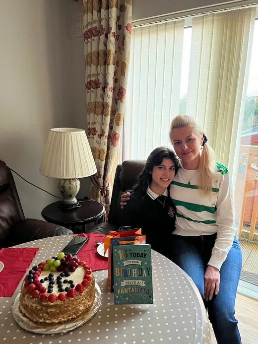 Chica junto a su madre anfitriona ante una tarta de cumpleaños con el número dieciséis
