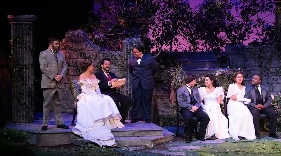 Una cerimonia di nozze formale si svolge all'aperto nell'area del Golden West College davanti a uno sfondo verde e viola.