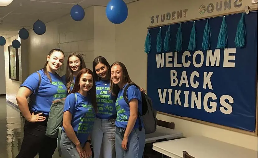 Estudiantes de la Gonzaga High School están sonriendo en el pasillo del colegio frente a una pancarta de bienvenida con globos azules.