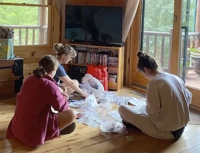 Tres mujeres sentadas en el suelo de madera organizando objetos en bolsas de plástico
