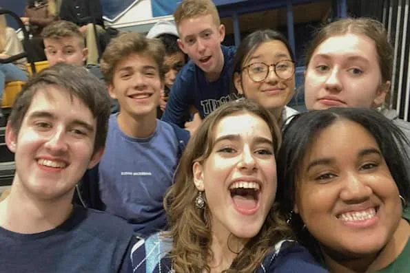 Grupo de jóvenes sonrientes posando juntos para un selfie en las gradas del pabellón