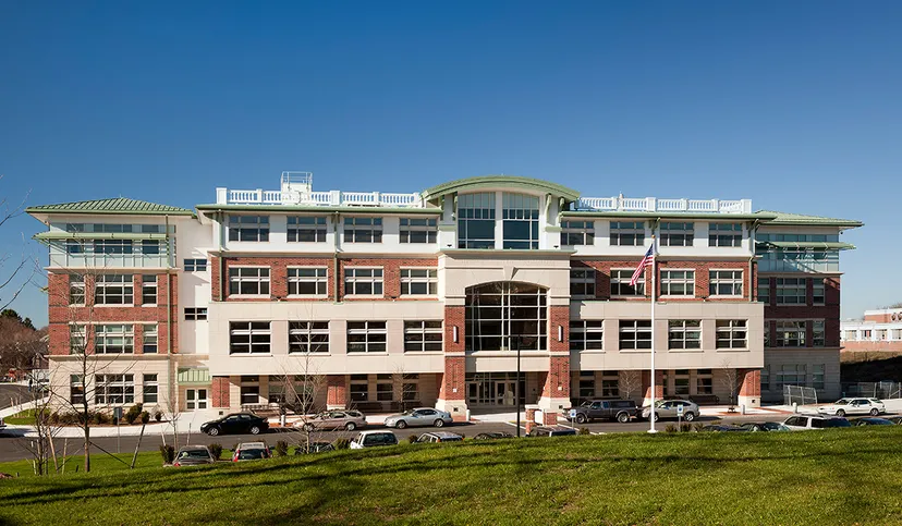 L'edificio a più piani della Beverly High School è circondato da un'area verde e auto parcheggiate sotto un cielo azzurro e limpido.