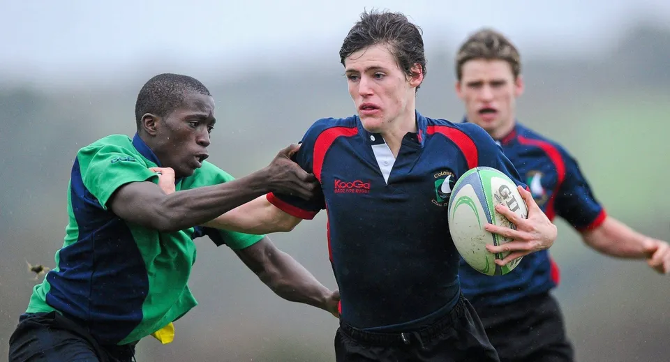 Due giocatori di rugby della Coláiste Chill Mhantáin eseguono un placcaggio sul campo in erba.